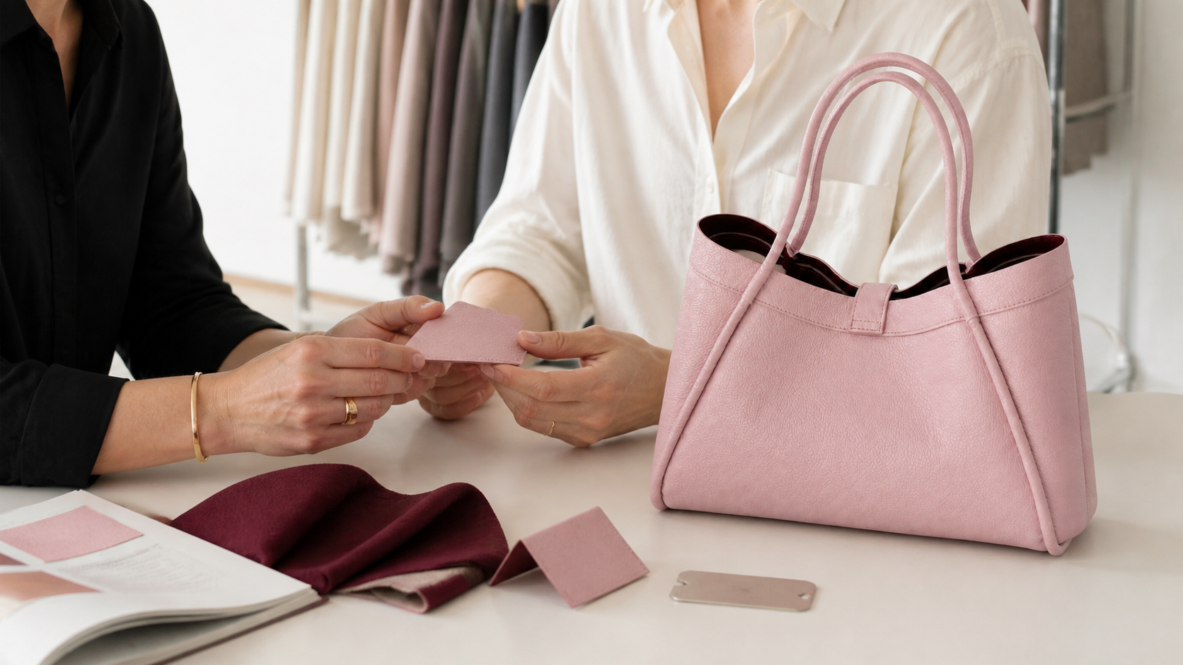 A client and leather-goods maker reviewing a sample bag and material swatches